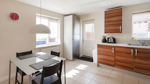 Eine moderne Küche mit Esstisch, Stühlen, einem Kühlschrank, Holzschränken und einem Fenster.