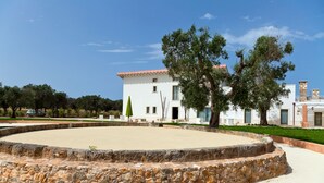 A courtyard with a stone wall, a white building with a red roof, and trees. - Masseria Sant'Eleuterio (Collepasso)