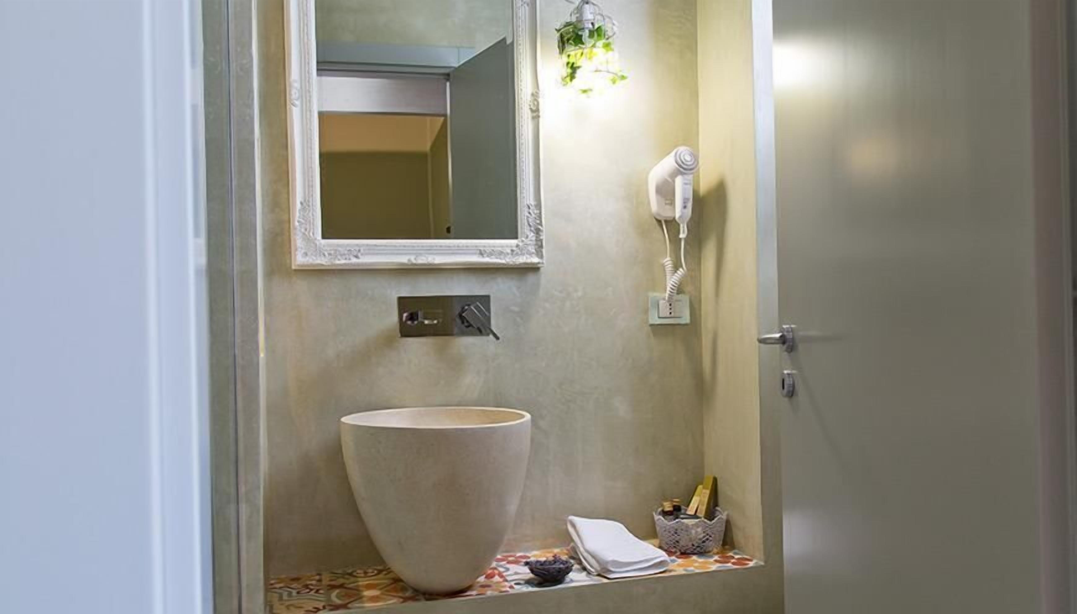 A bathroom with a large vessel sink, a mirror, a hairdryer, and a small basket with toiletries.