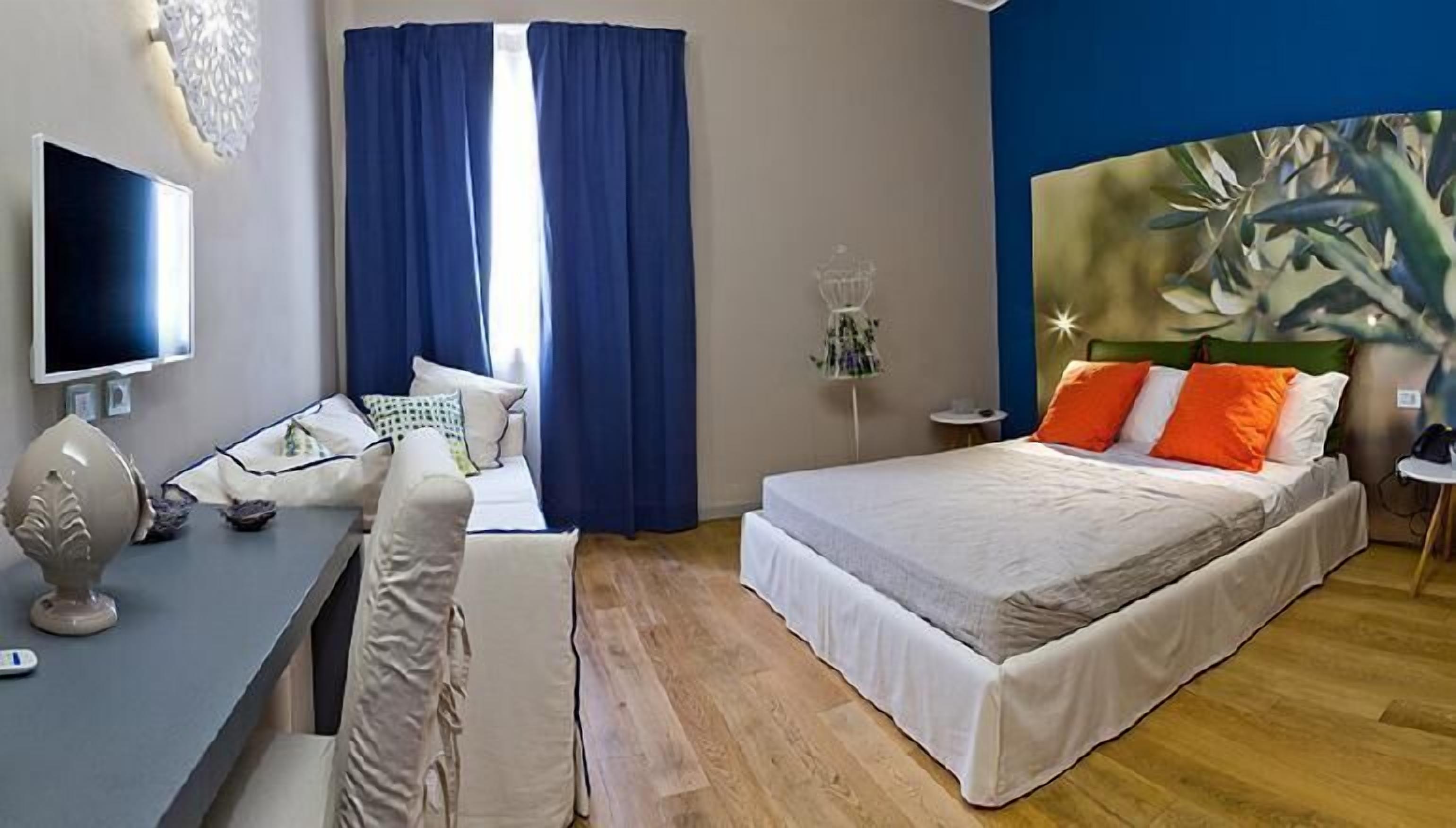A bedroom with a bed, a desk, a chair, a TV, and a painting on the wall.