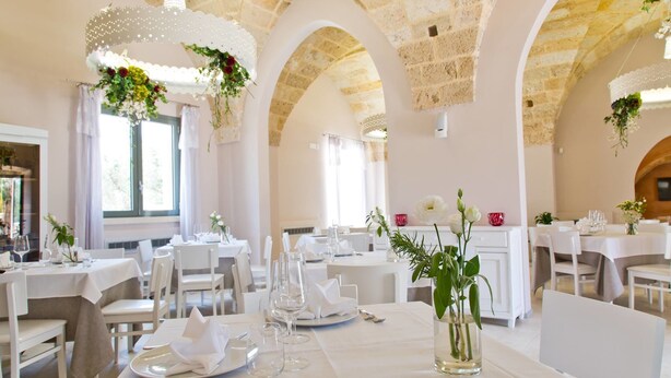 A restaurant with white tables and chairs, decorated with flowers and candles. - Masseria Sant'Eleuterio (Collepasso)
