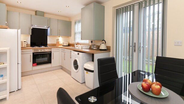 A modern kitchen with appliances, a dining area with a table and chairs, and a view through a glass door. - Condron 3 bedroom house (Worksop)