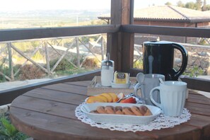 A wooden table with a white plate of food, a coffee pot, a mug, and a tea bag on a wooden deck with a view of a rural landscape. - Villaggio San Demetrio (Carlentini)