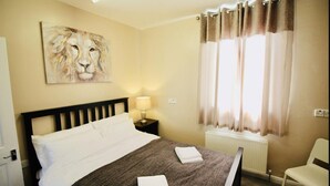 A hotel room with a bed, a nightstand with a lamp, a chair, and a painting of a lion on the wall.