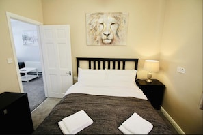 A hotel room with a bed, a painting of a lion, a nightstand with a lamp, and a door leading to another room. - Woodstock A 1 bed apartment (Belfast)