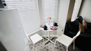 A small, compact room with a white table set for two, a black leather sofa, and a patterned floor.