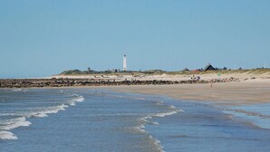 Paesaggio costiero con un faro, spiaggia sabbiosa e costa rocciosa.