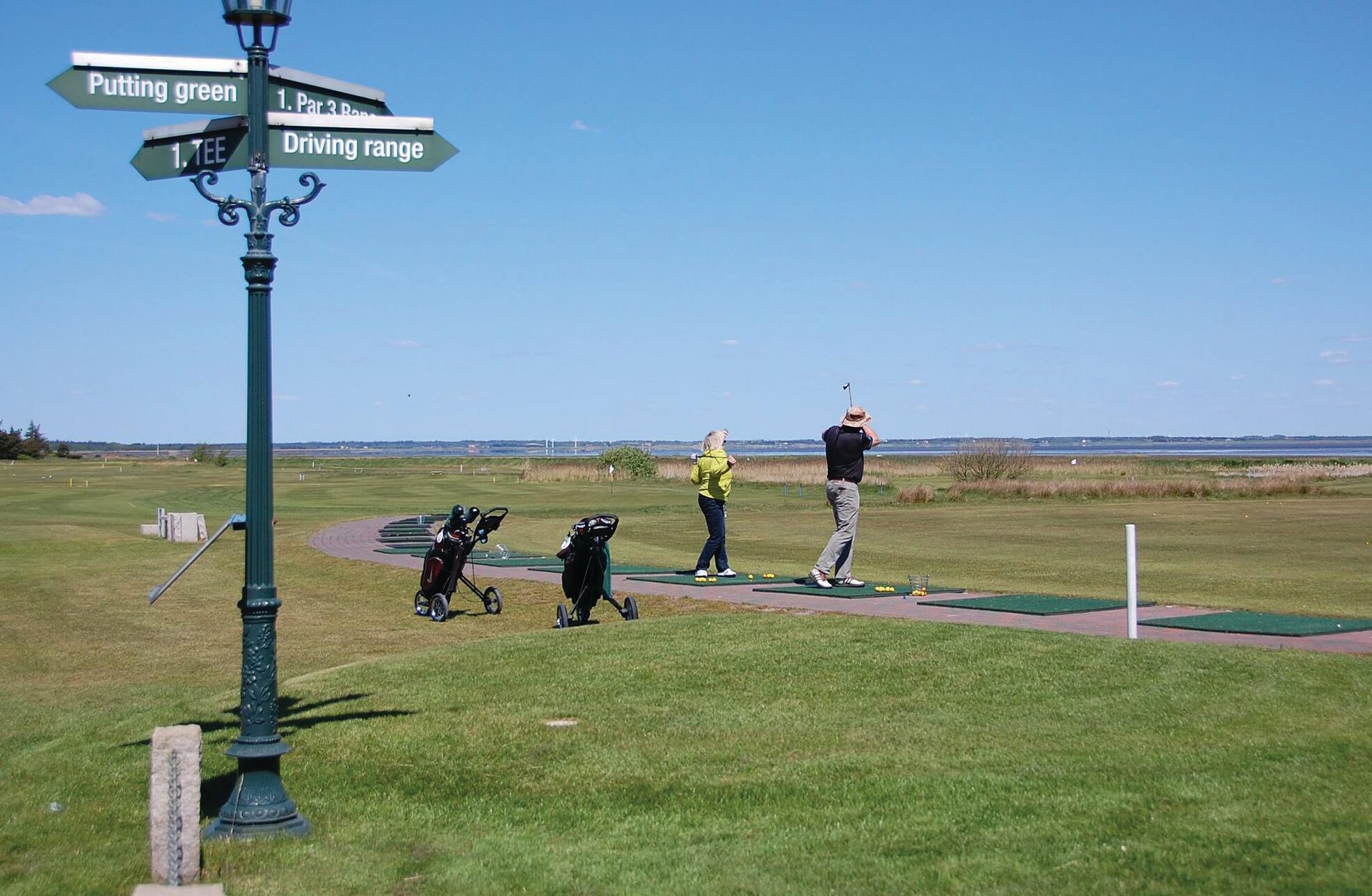 A golf course with directional signs, a putting green, and a driving range.
