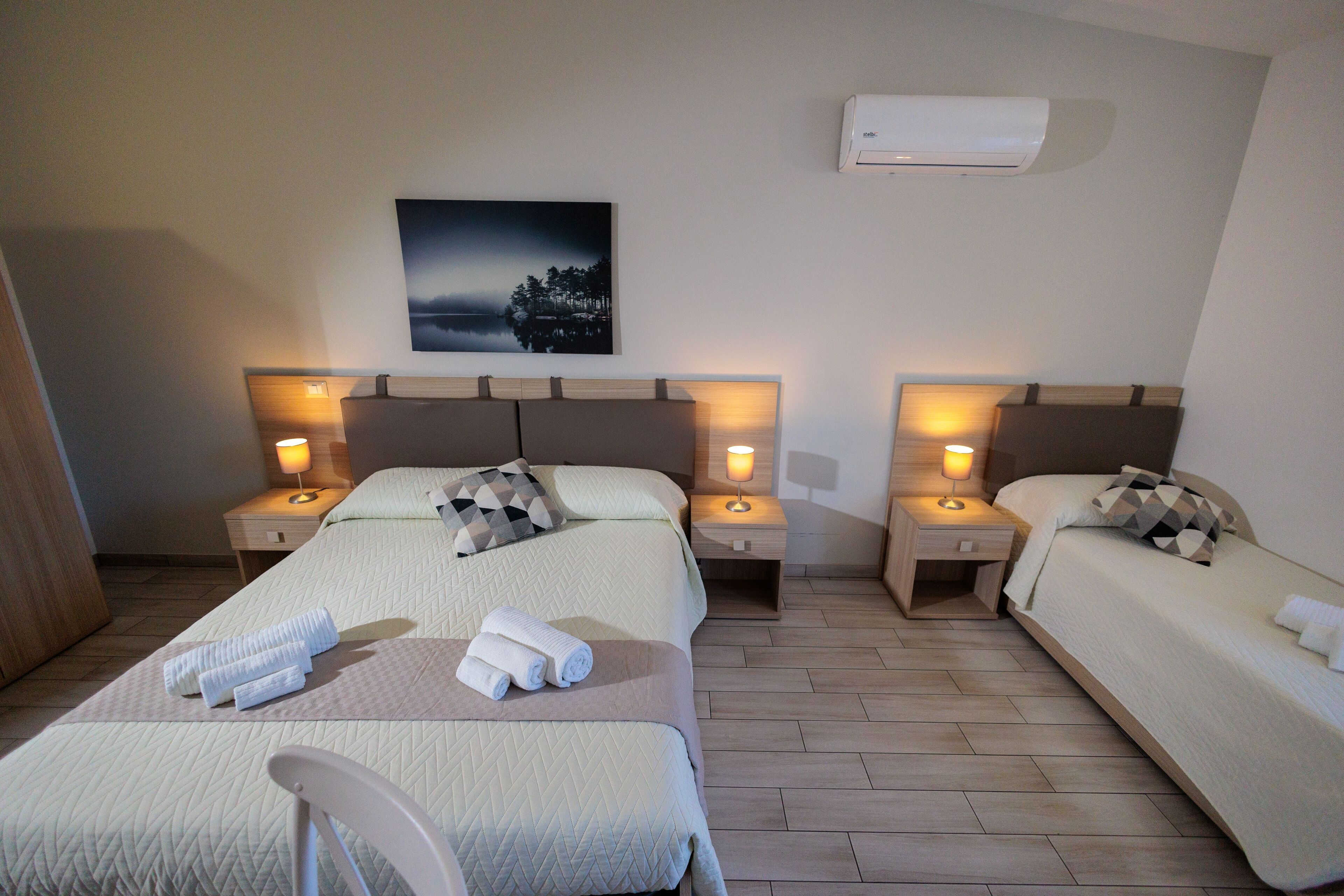 Een hotelkamer met twee bedden, een stoel, een nachtkastje met lamp en een wandairconditioner.