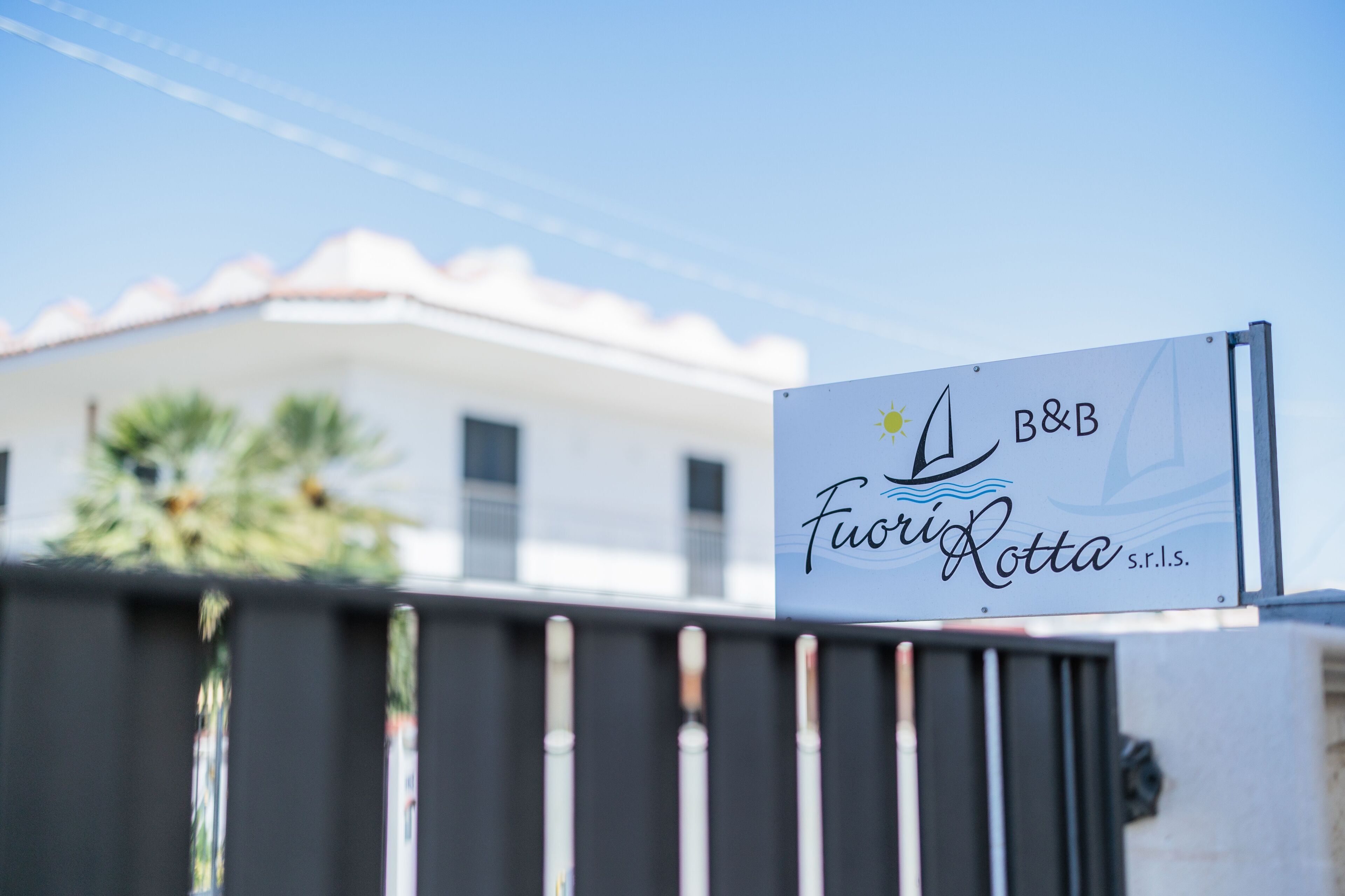 A sign for "Fiori Rotta s.r.l." with a sun and wave design, mounted on a metal gate.