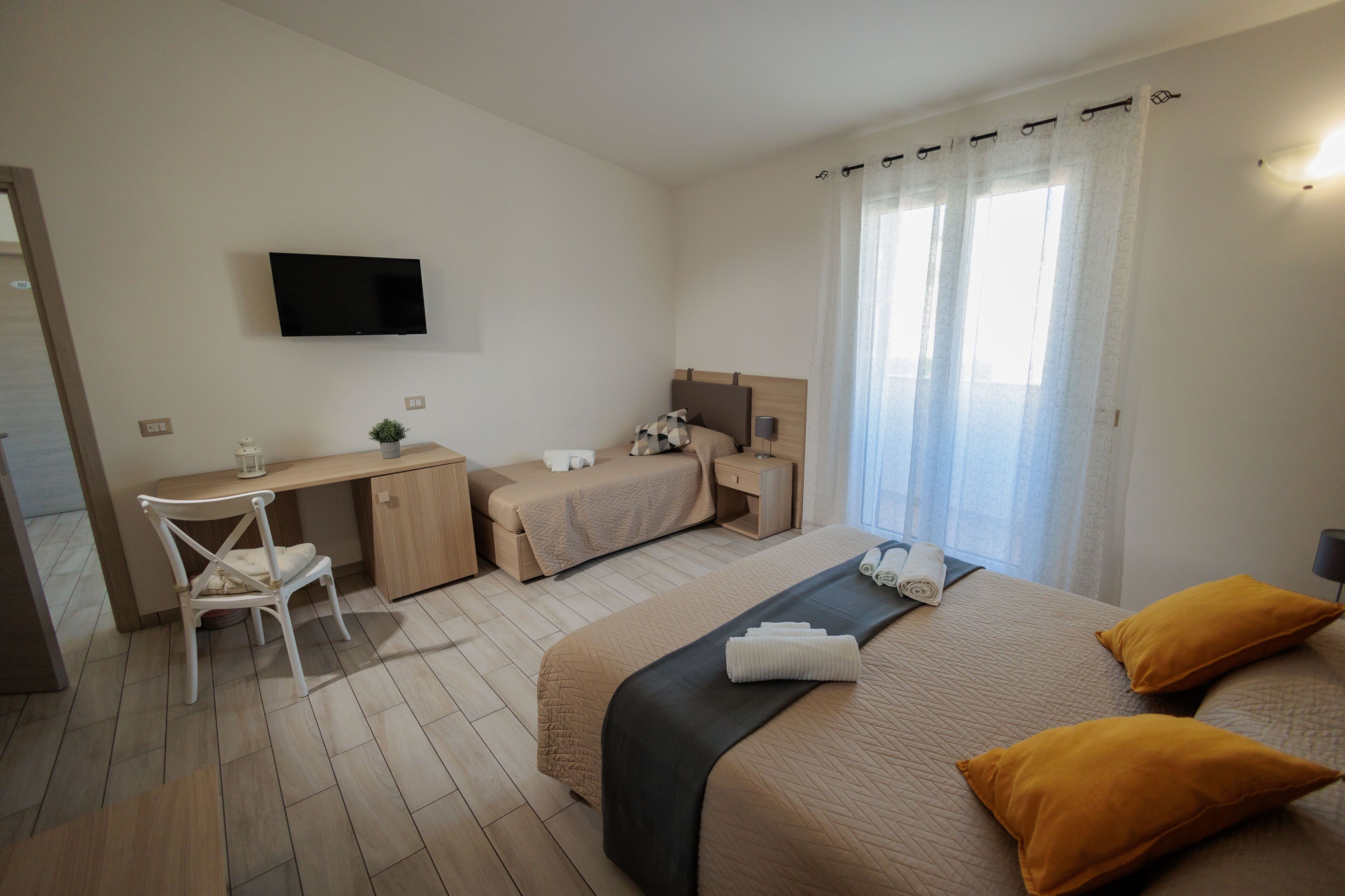Une chambre d’hôtel avec un lit, un bureau, une chaise, une télévision et une fenêtre avec des rideaux.