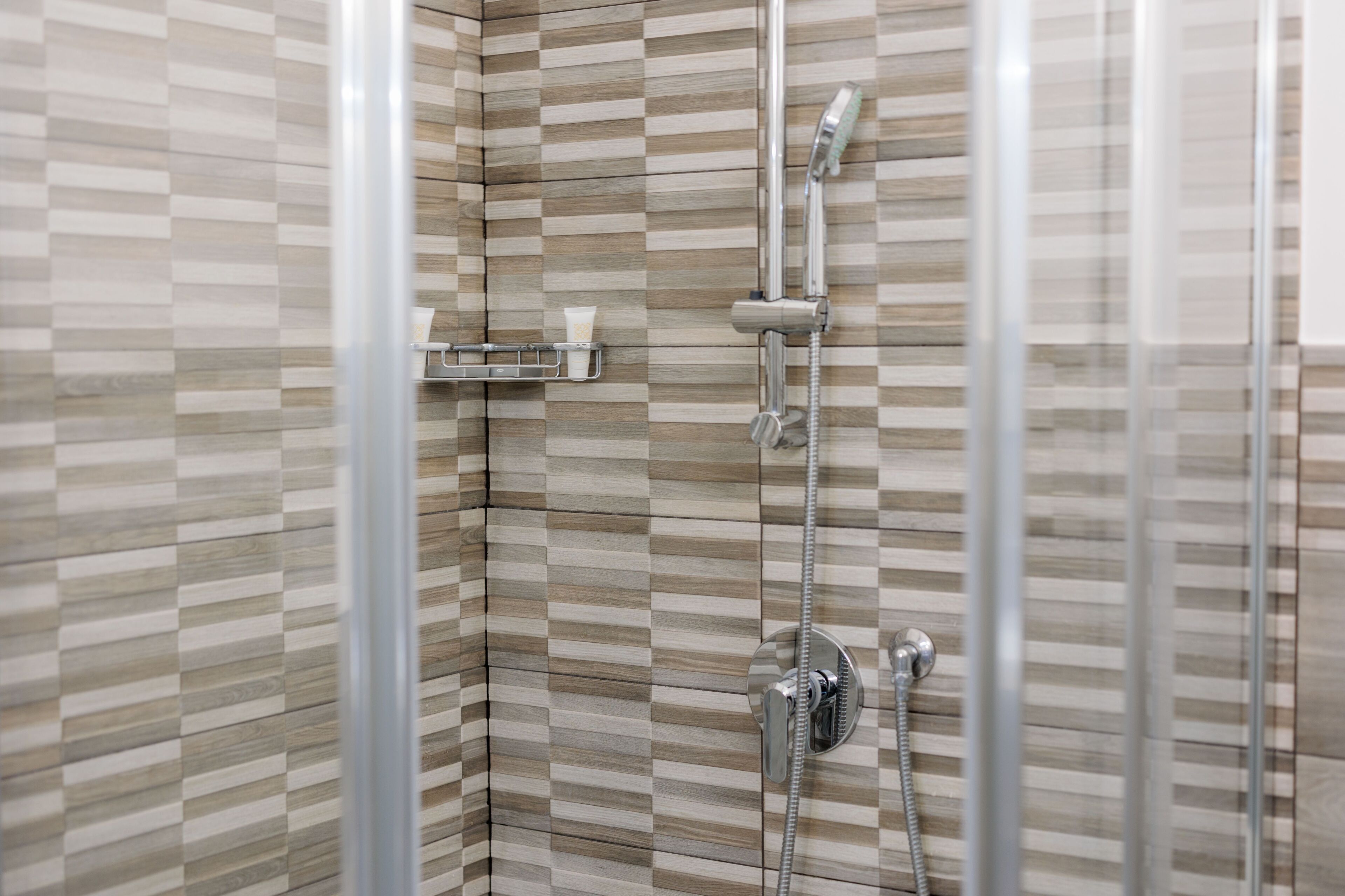 A shower with a glass door, a towel rack, and a soap dispenser.