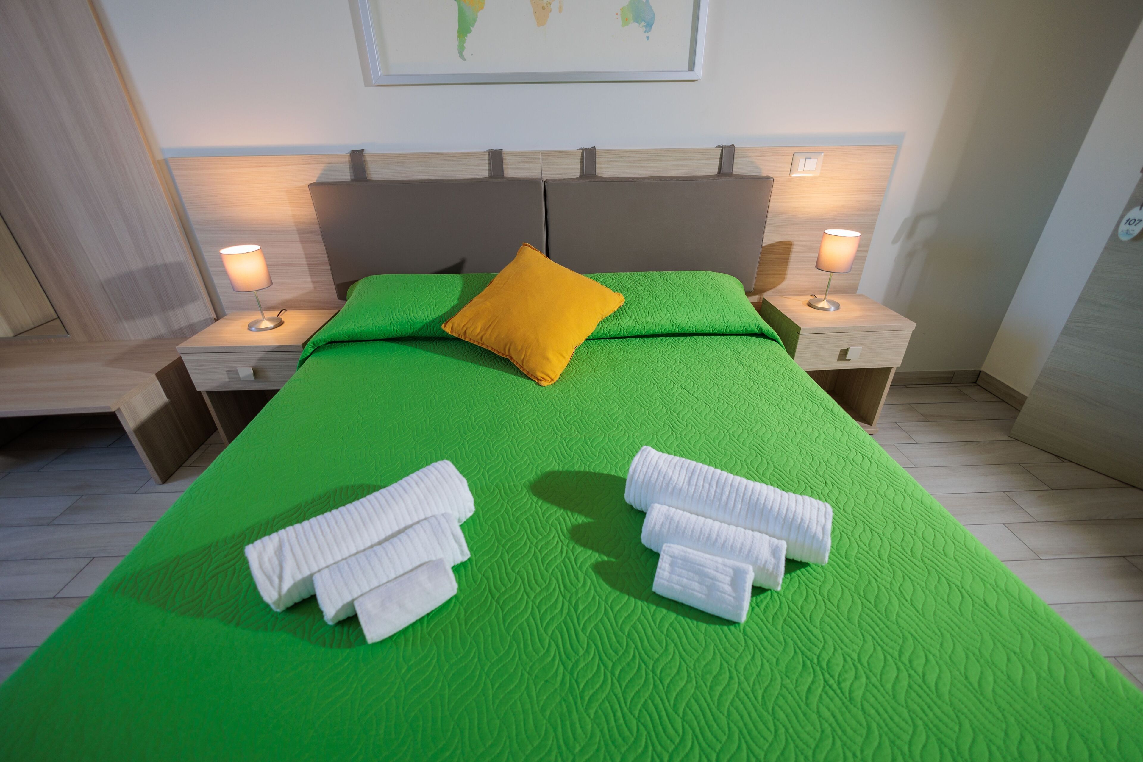 A hotel room with a green bedspread, a yellow pillow, and two bedside lamps.