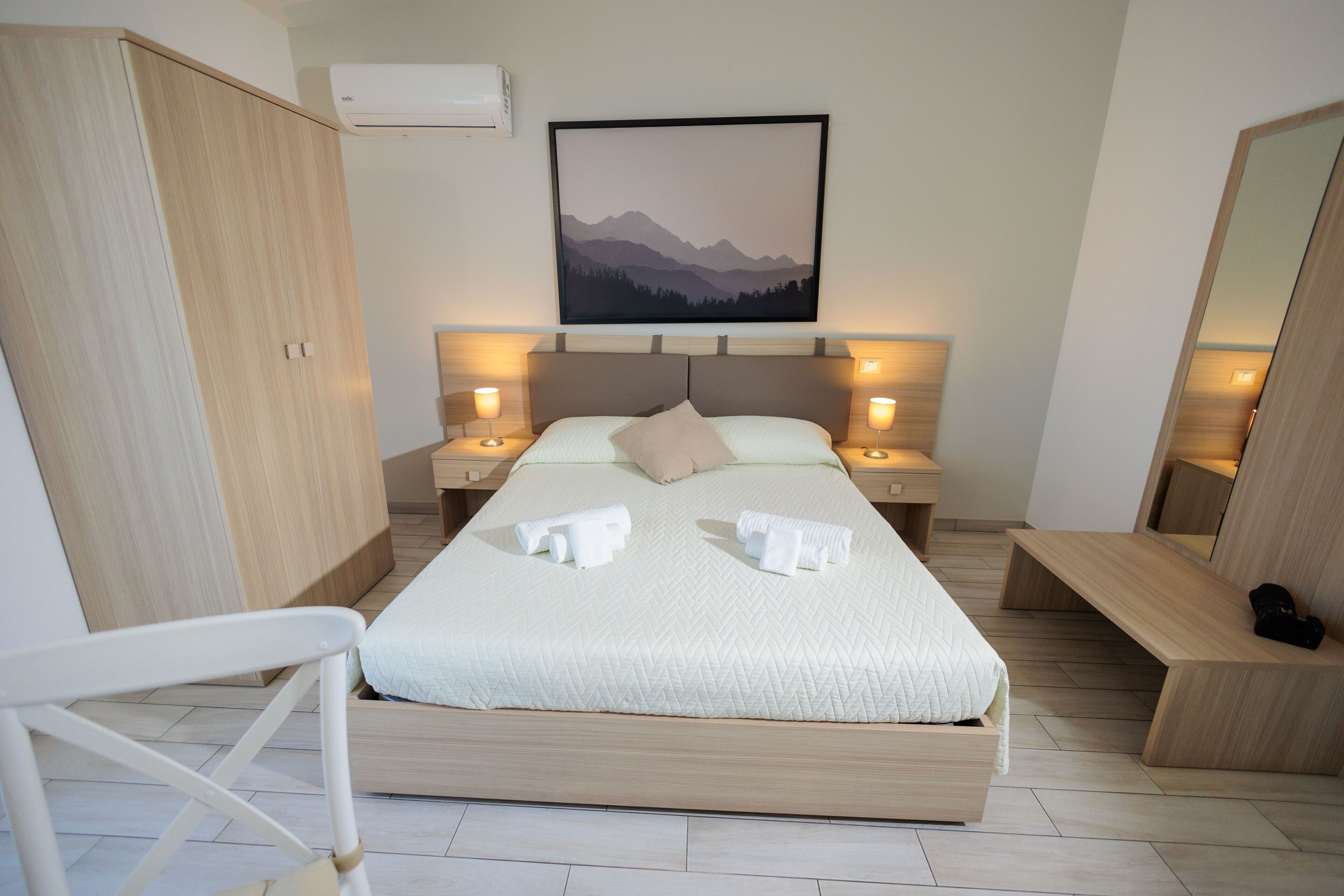 Een moderne slaapkamer met een groot bed, bedlampjes, een hoofdbord, een kledingkast, een bankje en een ingelijste foto aan de muur.