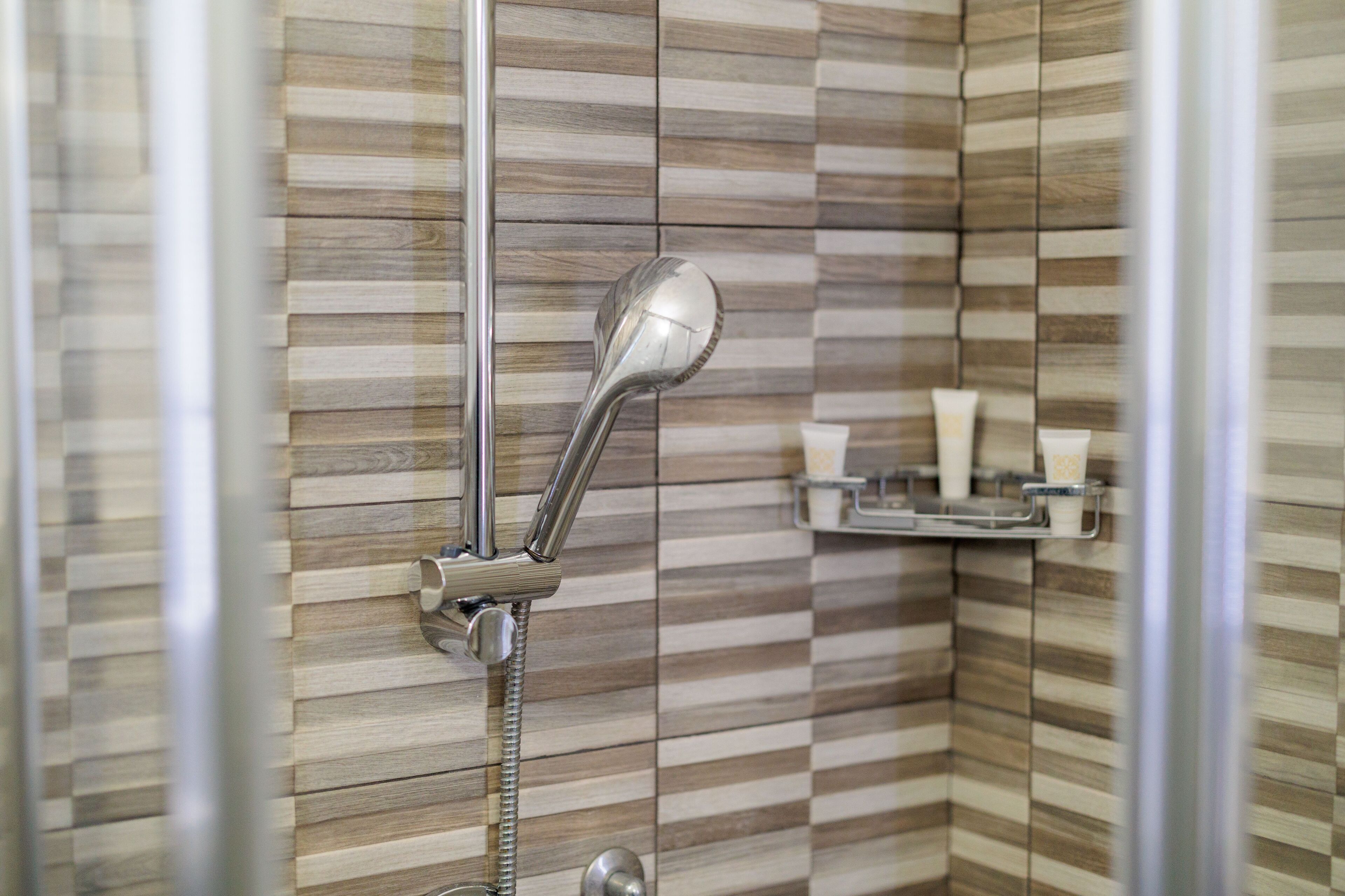 A shower with a chrome showerhead and a wall-mounted shelf with toiletries.