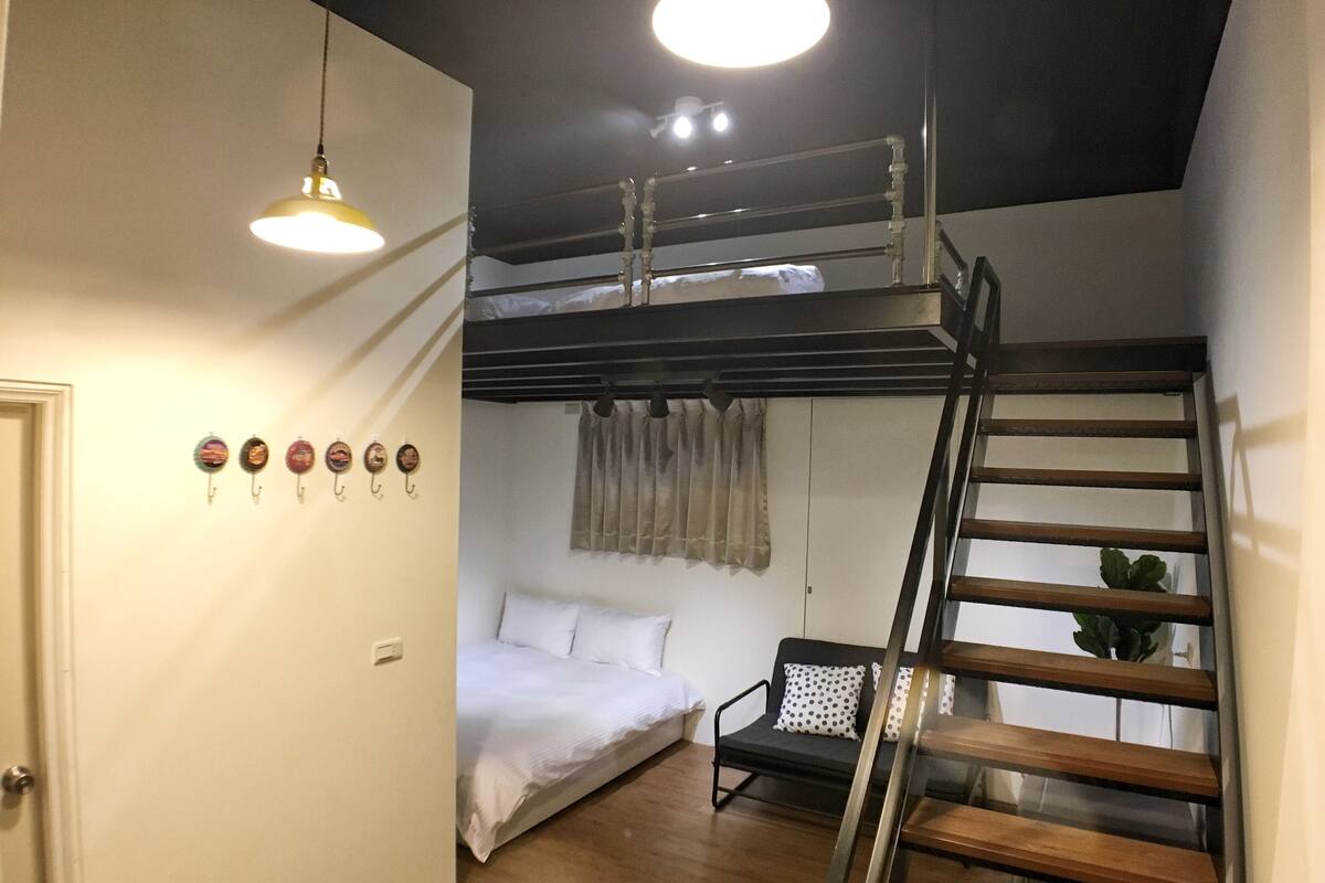 A compact room with a bunk bed, a desk, a chair, and a staircase.