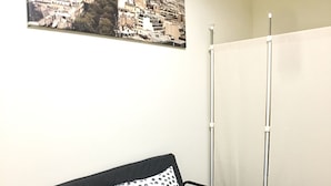 Una habitación con un sofá negro, dos almohadas de lunares, un cuadro con la Torre Eiffel y una partición blanca.