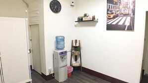 Un pasillo con un dispensador de agua, un reloj, un estante con objetos pequeños y un cuadro en la pared.