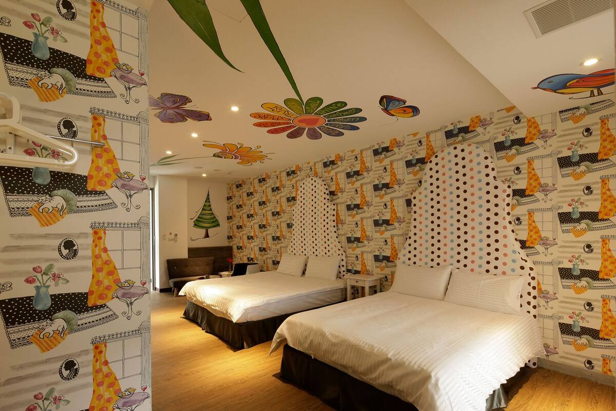 Un dormitorio con dos camas, una mesita de noche y un aparador. Las paredes están decoradas con un papel pintado con motivos y diseños variados.