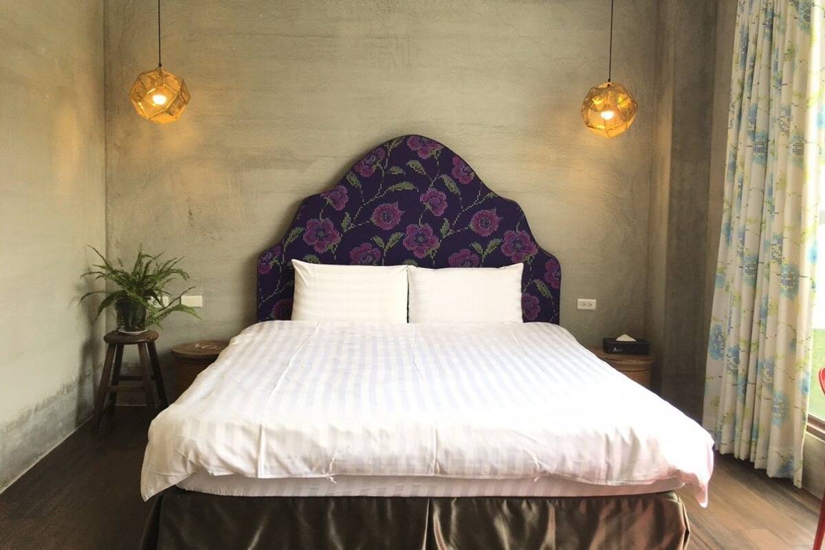 Un dormitorio con una cama, dos lámparas colgantes, una planta en maceta y una cortina.