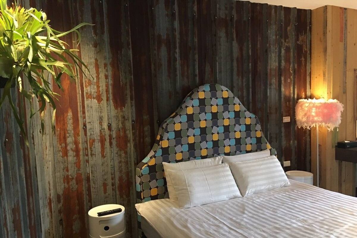 Un dormitorio con un cabecero estampado, una lámpara de noche y una planta.
