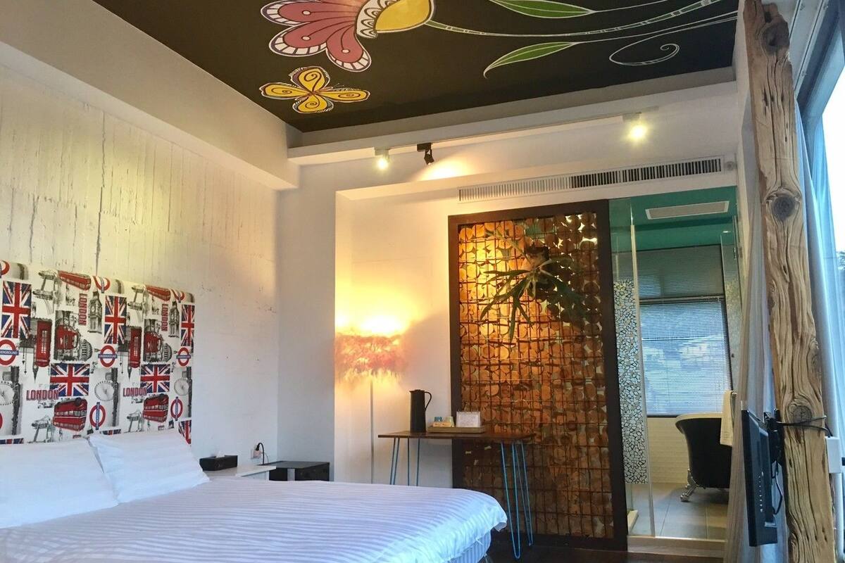 Una habitación de hotel moderna con una cama, una pared decorada con una obra de arte sobre Londres, un techo decorativo y vistas al exterior.