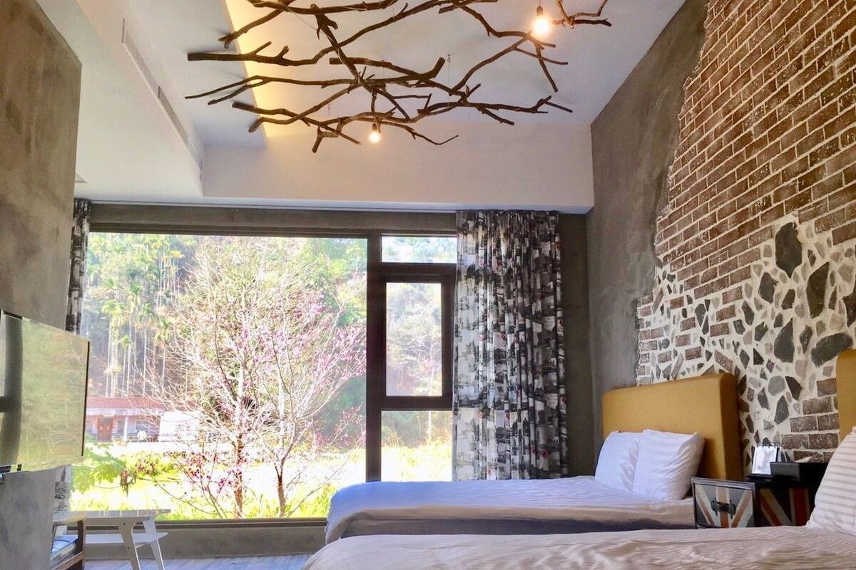 Un dormitorio moderno con dos camas, un ventanal con vistas a árboles y una lámpara de techo original con forma de rama.
