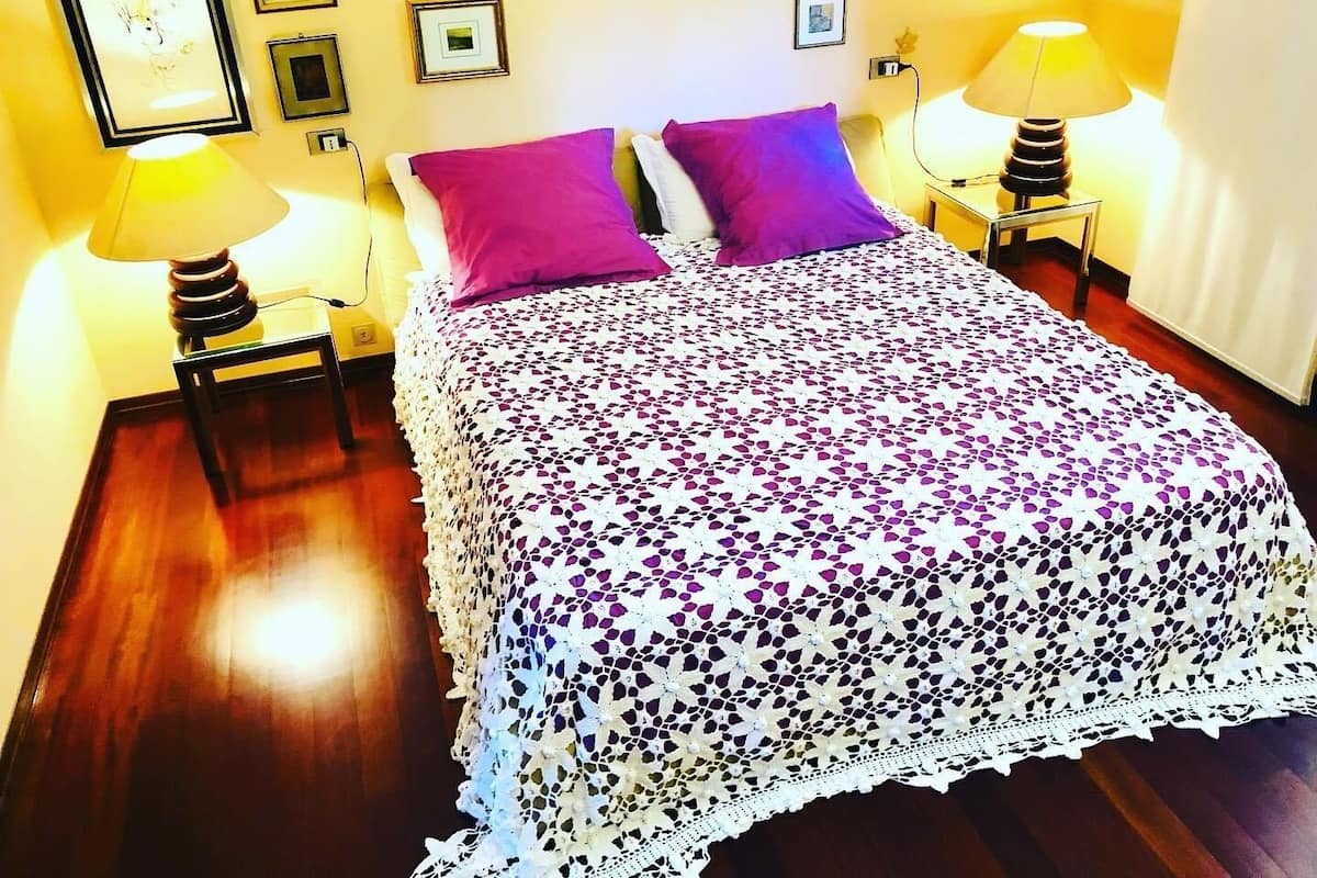 Ein ordentlich gemachtes Bett mit einem gemusterten Bettbezug und zwei Kissen, begleitet von zwei Nachttischlampen auf Holznachttischen.