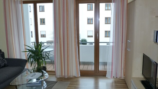 A living room with a glass coffee table, a sofa, a TV, and a balcony with curtains. - Abendsonne (Bamberg)