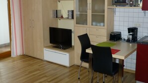 A compact kitchen with a microwave, toaster, and coffee maker. There is a TV on a stand and a cabinet with glass doors. - Abendsonne (Bamberg)