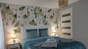 A bedroom with a bed, two bedside tables, a nightstand, a wall with leaf patterns, and a door with glass panels. - Aux Agapanthes (Pluherlin)