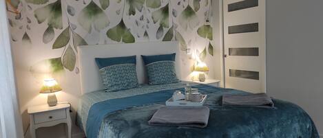Ein Schlafzimmer mit einem Bett, zwei Nachttischen, einer Kommode, einer Wand mit Blattmustern und einer Tür mit Glasfeldern.