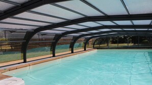 An indoor swimming pool with a glass ceiling and wooden deck. - Aux Agapanthes (Pluherlin)