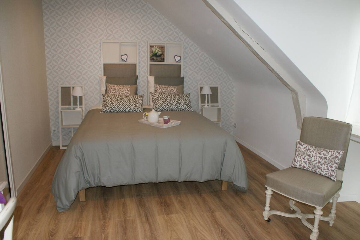 Un dormitorio con una cama, dos mesitas de noche, una silla y una pared decorativa con motivos geométricos.