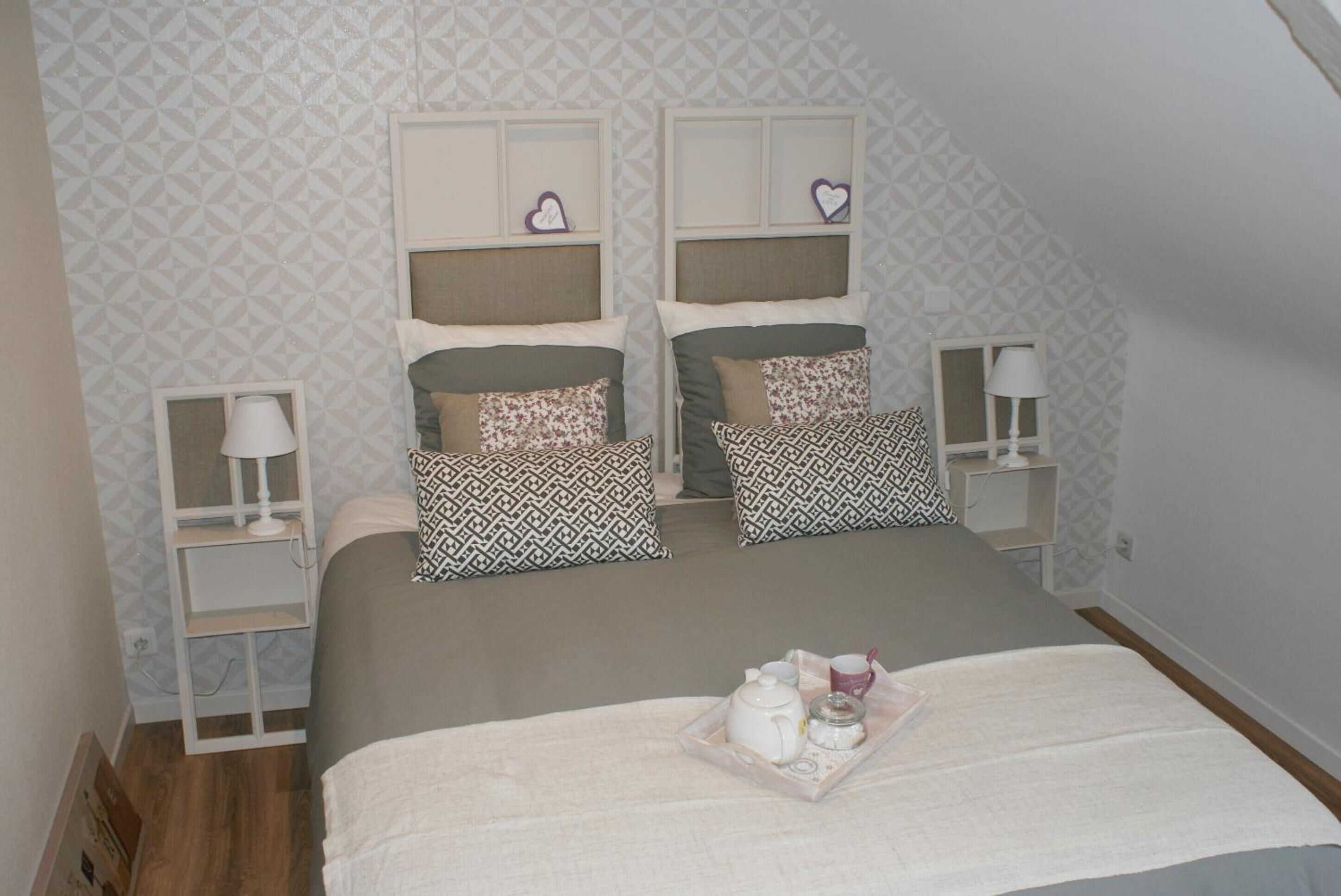 A bedroom with two beds, each with a headboard, bedside tables, and decorative pillows. There is a tray with tea and cups on the bed.