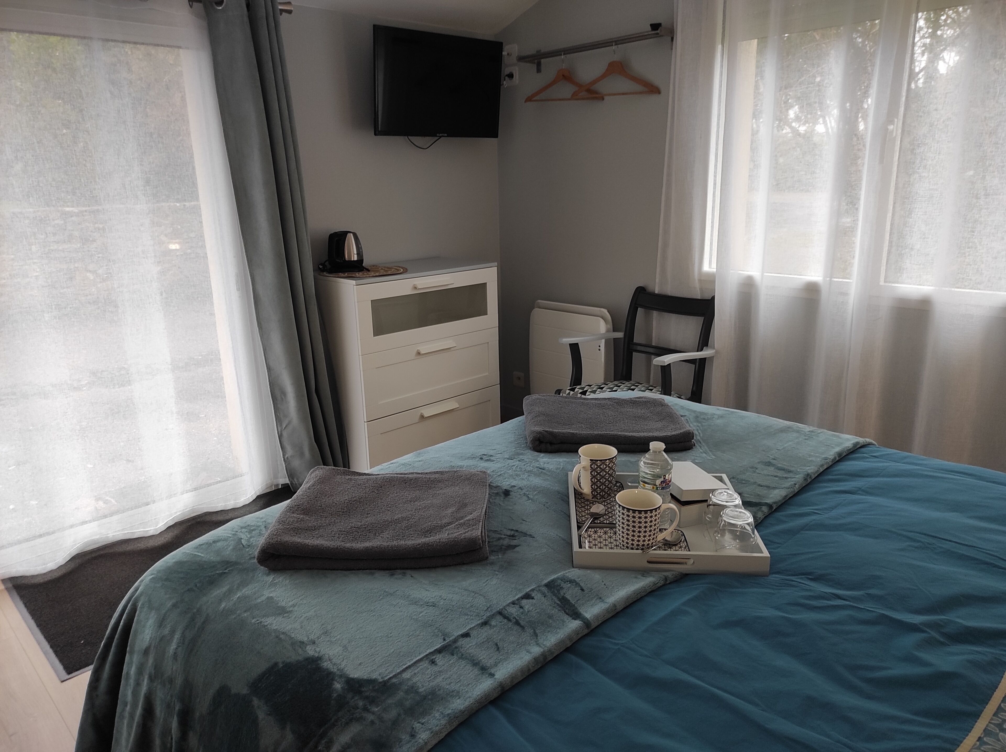 Ein ordentlich bezogenes Bett mit einem Frühstücksbrettchen, ein Nachttisch mit einer Lampe, ein Stuhl und ein an der Wand befestigter Fernseher.