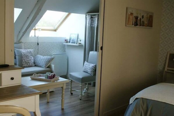 Una habitación acogedora con una cama, un escritorio, una silla y un sofá. Hay un tragaluz sobre el sofá y una ventana con cortina.