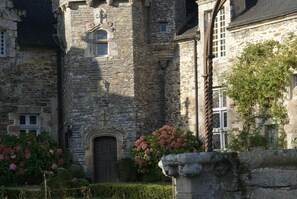 A stone building with a central arched doorway, surrounded by hedges and flowering plants. - Aux Agapanthes (Pluherlin)