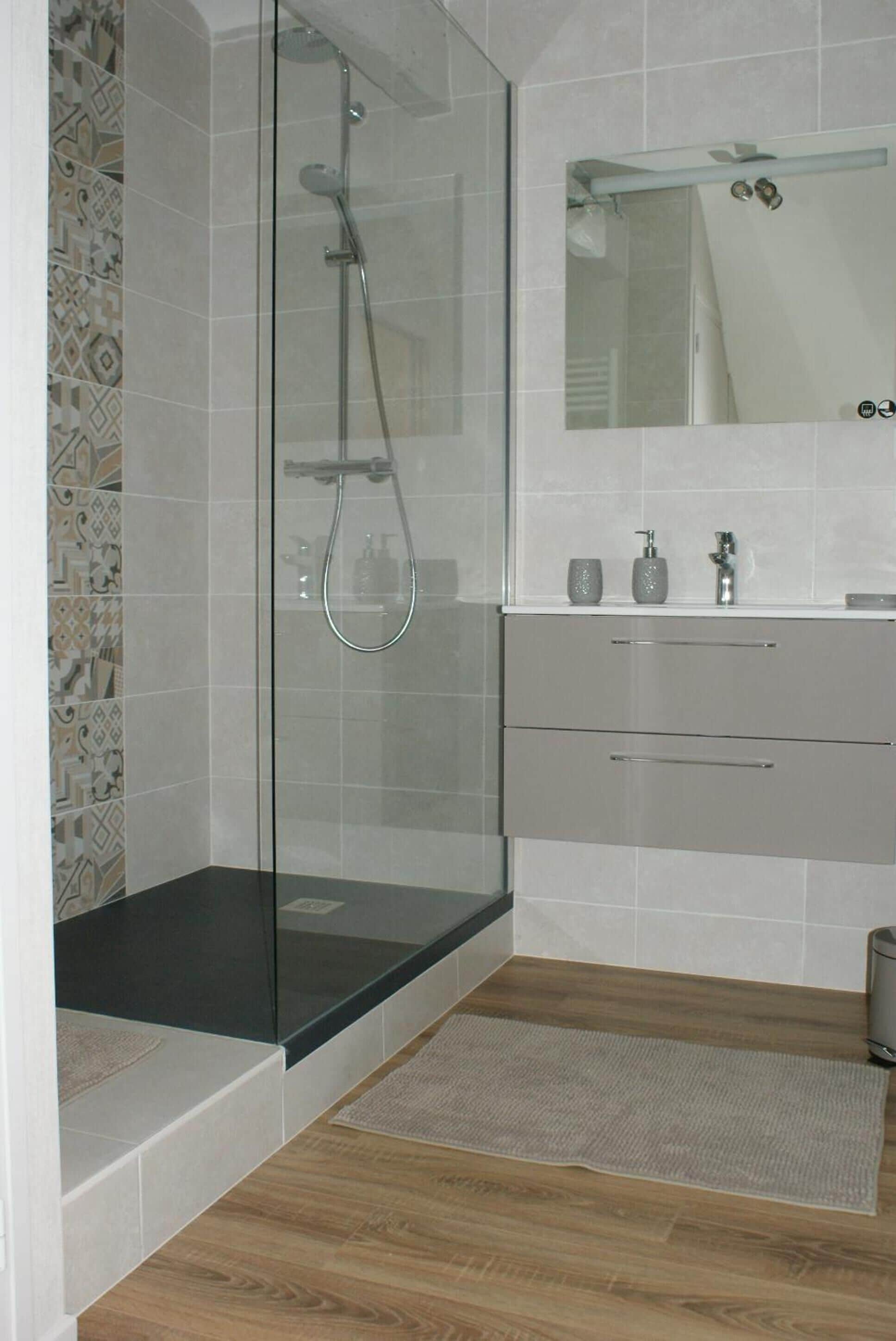 Un baño moderno con ducha de vidrio, tocador con espejo y salpicadero de azulejos estampados.