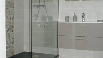 Un baño moderno con ducha de vidrio, tocador con espejo y salpicadero de azulejos estampados.