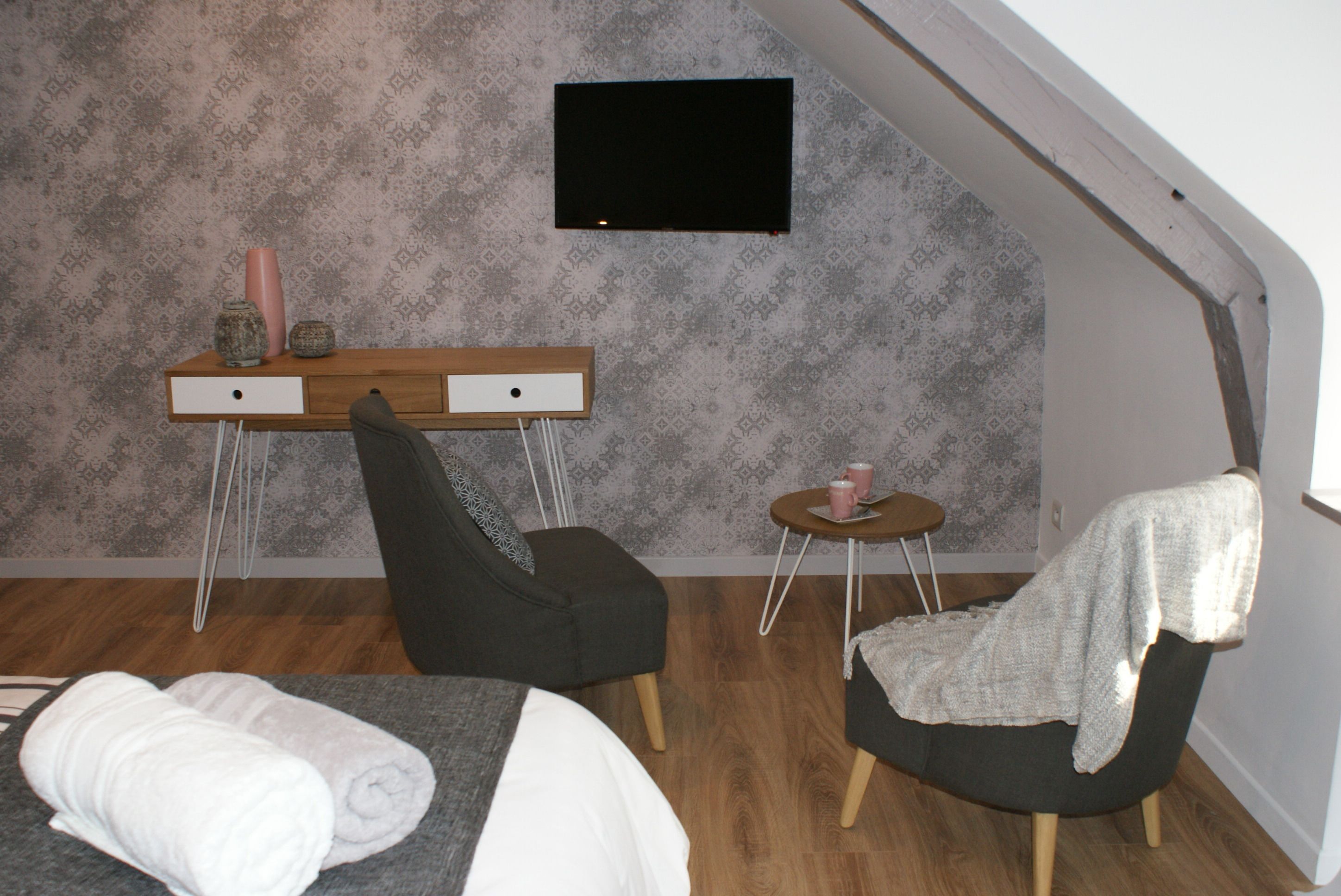 A compact room with a bed, a desk, two chairs, and a small table with a cup.