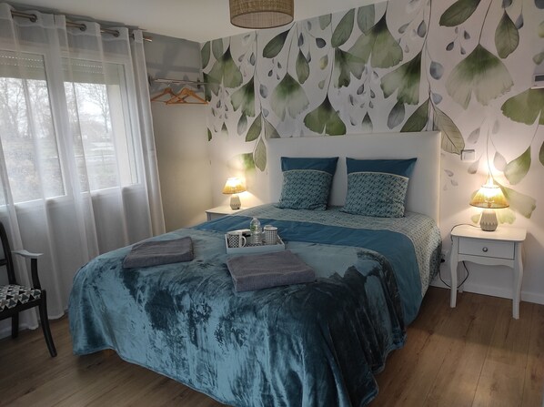 Une chambre à coucher avec un grand lit, deux tables de chevet, une chaise et une fenêtre ornée de rideaux légers.