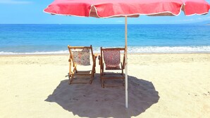 Une plage avec un parasol rouge et deux chaises en bois.