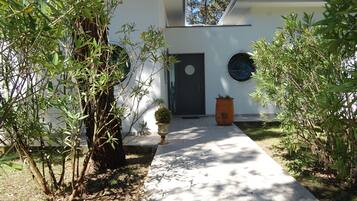 Stylish entrance with a black door, flanked by lush greenery and potted plants.