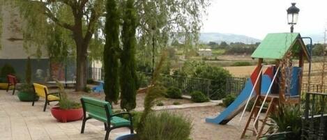 Un espace de jeux pour enfants avec un toboggan, des bancs et des plantes en pot.