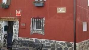 A red building with a stone base, a small outdoor seating area, and a sign indicating a public space.