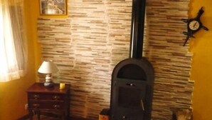 A room with a stone-patterned wall, a fireplace, a clock, and a small table with a lamp.