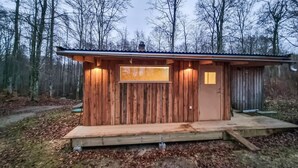 A small wooden cabin with a single door and window, surrounded by a forest.
