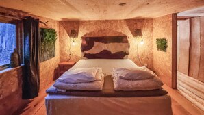 A cozy bedroom with a wooden headboard, a large bed with two pillows, a nightstand, and a wall-mounted lamp.