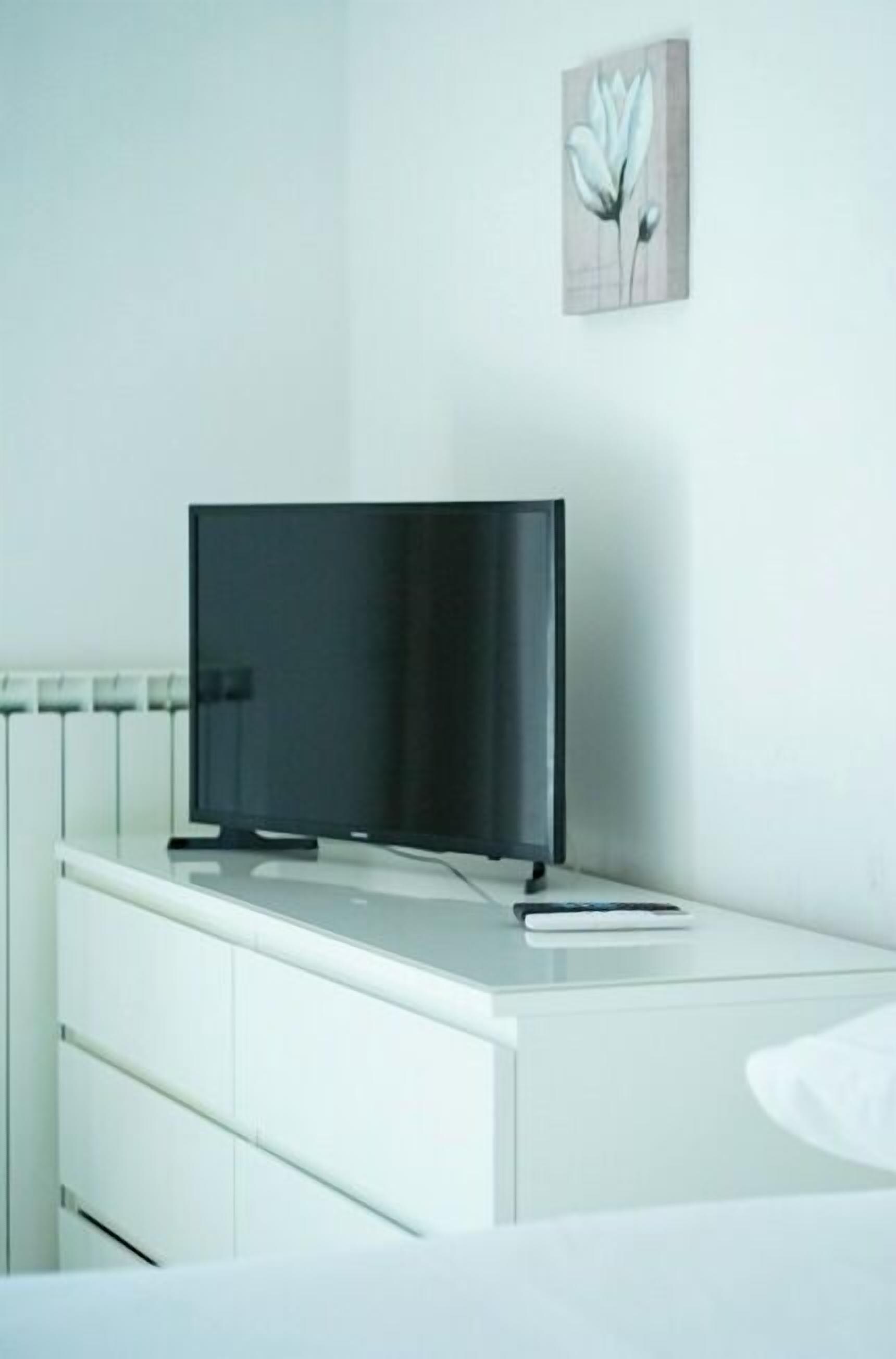 A modern room with a flat-screen TV on a white dresser, a radiator, and a wall-mounted artwork.
